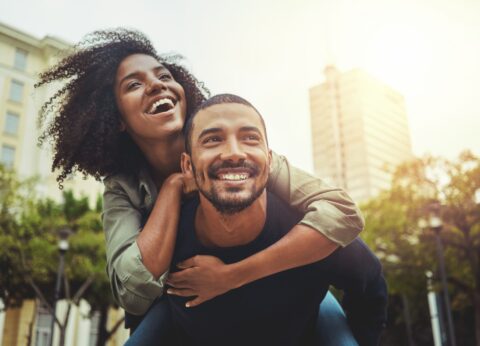 A young happy couple where a man is giving a woman a piggyback ride in the city